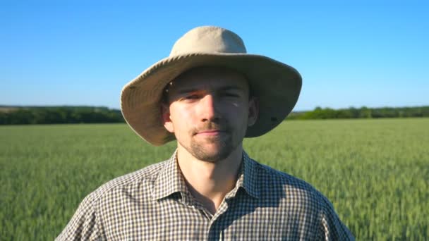 有信心的农夫的肖像看着在绿色麦田背景的相机 在阳光明媚的夏日 站在草地上的穿着衬衣的年轻人关门了 — 图库视频影像