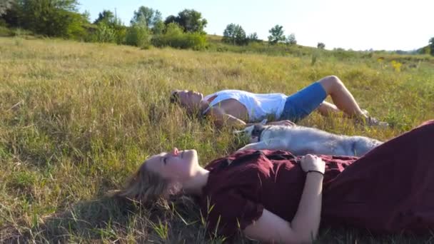 Dolly tiro de jovem casal apaixonado deitado na grama verde no campo e acariciando seu cão husky siberiano no dia ensolarado. Feliz par relaxar e desfrutar de fim de semana de verão ao pôr do sol. ângulo baixo vista Fechar — Vídeo de Stock