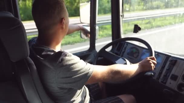 Man holds hand on the steering wheel and driving truck through countryside on a warm summer day. Profile of truck driver. Trucker inside at car. Side view Close up Slow motion Stock Video
