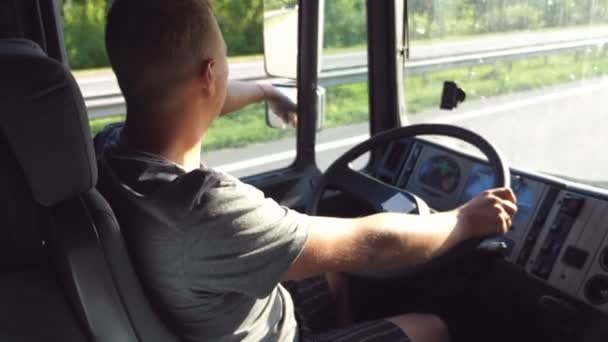 Man holds hand on the steering wheel and driving truck through countryside on a warm summer day. Profile of truck driver. Trucker inside at car. Side view Close up Slow motion — Stock Video