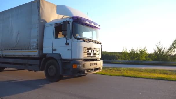 Camera volgt naar de vrachtwagen rijden op snelweg in avond. Vrachtwagen rijdt door platteland met zonsondergang op de achtergrond. Bestuurder rijdt op hoge snelheid. Close up van de cabine van de vrachtwagen. Zijaanzicht Slow motion — Stockvideo