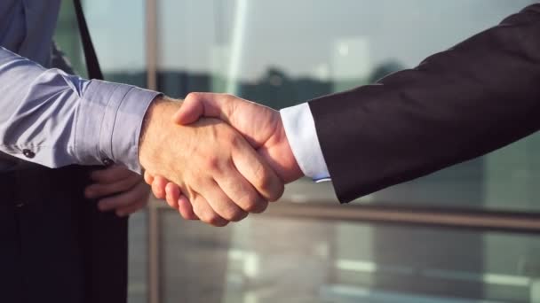 Dolly shot of two businessmen shaking hands after successful deal near office building. Close up of young colleagues congratulating each other in urban environment. Handshake of business partners — Stock Video