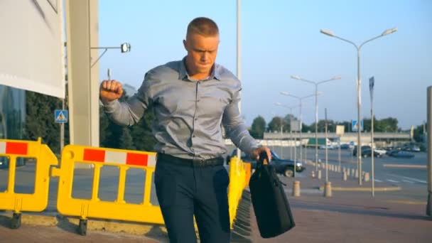 Close up of cheerful young businessman with briefcase funny dancing while walking near airport terminal at sunset. Happy handsome man in shirt with bag celebrating his achievement and success — Stock Video