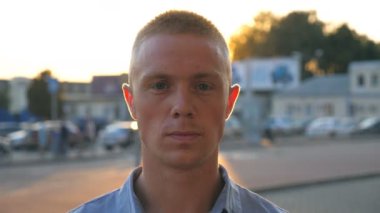 Kameranın on sunset Park Arabalar arka planı bakarak gömlekli genç ciddi işadamı portresi. Bir kentsel ortamda ayakta emin başarılı adam yakın çekim