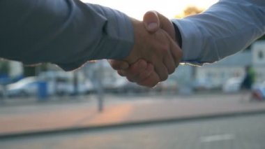 Otoparkın arka planında birbirini selamlayan iki başarılı iş adamına yakın çekim. Gün batımında şehir sokağında genç meslektaşlar buluşup el sıkışıyor. İş tokalaşması.