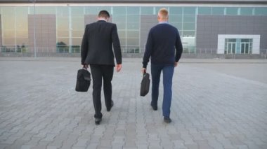 Formal giyim çanta ile office merkezine gidiş iki tanınmaz halde Genç İşadamları. Şehirde iş ile kendine güvenen yöneticileri ile çanta olacak. Çalışmaya commuting başarılı iş arkadaşları. Arkadan Görünüş