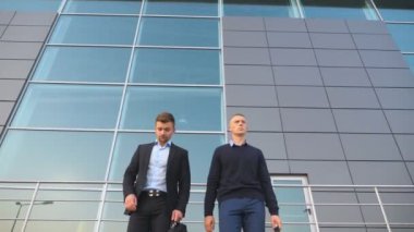 Formal giyim inşaat işleri sonra ofisinden evrak çantaları ile yürüyen iki genç başarılı meslektaşlarının düşük açılı görünüş. Yakışıklı işadamları ile çanta iş City ev peşinde. Yakın çekim