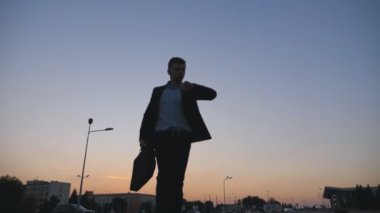 Düşük açılı manzara resmi siyah elbiseli saatine bakıyor ve evrak çantası ile şehir sokak çalışan genç iş adamı. Yakışıklı adam gün batımında önemli toplantı için geciktim. Yakın çekim