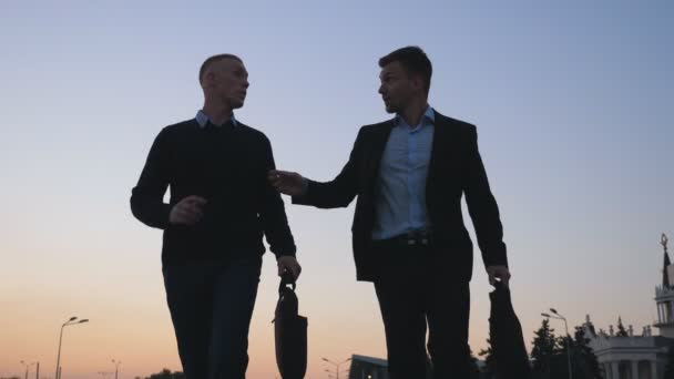 Close-up de dois jovens empresários felizes com pastas engraçadas dançando enquanto caminhava após negócio bem sucedido na rua da cidade. Colegas alegres celebrando a realização ao pôr do sol. Vista de ângulo baixo — Vídeo de Stock