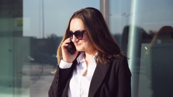 Portrait d'une jeune femme d'affaires souriante parlant au téléphone. Joyeux belle femme parlant sur smartphone près du centre d'affaires moderne. La femme d'affaires est de bonne humeur. Ralenti Fermer — Video