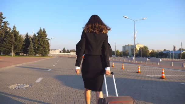 Business woman with her suitcase going from airport to taxi parking. Lady walking with her luggage along city street. Female legs in high heels stepping at sidewalk. Rear back view Slow motion — Stock Video