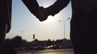 İki mutlu arkadaşları birbirlerini otopark arabalar arka planı tebrik. Toplantı ve city adlı sokak sunset Bulvarında tokalaşırken genç başarılı işadamları. Vinç ağır çekim yan görünüm vurdu