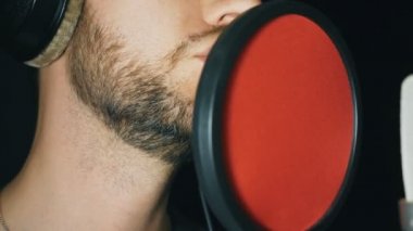 Erkek şarkıcı şarkı ses stüdyosunda ağzı. Tanınmayan adam kayıt yeni şarkı. Sakallı adam mikrofon için şarkı söyler. Yaratıcı müzisyen çalışma. Koyu arka plan. Ağır çekim yakın çekim