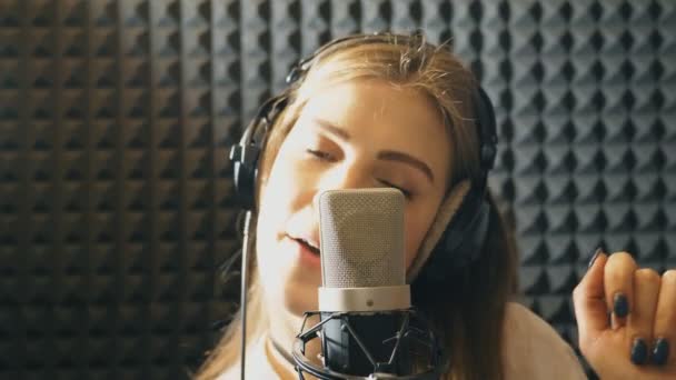 Stüdyoda şarkı söyleyen güzel bir kızın portresi. Genç şarkıcı duygusal olarak yeni bir şarkı kaydediyor. Bayan mikrofona şarkı söylüyor. Yaratıcı bir müzisyenin çalışması. Gösteri dünyası konsepti. Yavaş çekim. Yakın çekim.