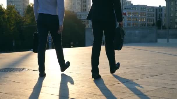 Dos hombres de negocios con maletines caminando por la calle de la ciudad con destellos de sol en el fondo. Los hombres de negocios viajan para trabajar juntos. Los tíos confiados están de camino a la oficina. Colegas van al aire libre. Lento mo — Vídeo de stock