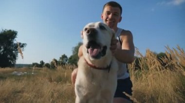 Genç adam çayır çim üzerinde oturur ve onun labrador vuruş. Adam onun evde beslenen hayvan içinde doğa ile birlikte vakit geçiriyor. Sevgi ve dostluk ile Evcil hayvan. Dolly atış yavaş hareket yakın çekim