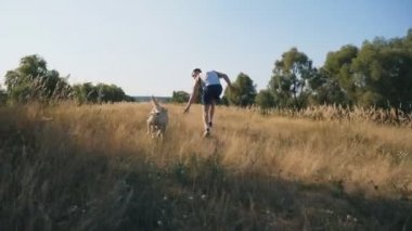 Genç adam açık havada onun labrador ile çalışır. Adam onun evde beslenen hayvan içinde doğa ile birlikte koşu. Evcil hayvan sahibi izler. Arka plan, güzel manzara. Arkadan görünüm yavaş hareket yakın çekim