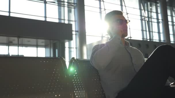 Primer plano retrato del hombre de negocios guapo serio en gafas de sol hablando por teléfono celular en la oficina. Joven hombre de negocios hablando por teléfono en el aeropuerto con destello de sol en el fondo. Movimiento lento — Vídeo de stock