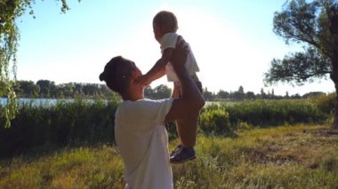 Profili bir genç baba oğlunun elinde Park'ta bir güneşli yaz gününde yükseltir. Mutlu baba ve sevimli çocuğunu doğa birlikte vakit sarı saçlı. Yan görünümü ağır çekim yakın çekim