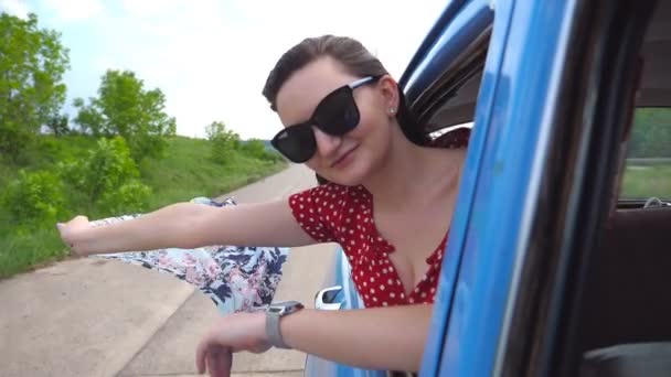 Chica joven con bufanda en las manos apoyada en la ventana del coche vintage y disfrutando del paseo. Retrato de mujer atractiva mira hacia fuera de coche retro en movimiento. Concepto de viaje y libertad Cámara lenta Primer plano — Vídeo de stock