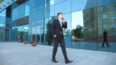 Genç işadamı telefonda konuşuyor ve başarıyı kutluyor. İş adamı cep telefonundan iyi haberler duymuş ve olumlu duygular besliyor. Erkek portresi başarıyla mutludur. Yavaş çekim