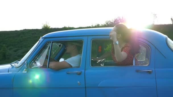 Menina atraente em óculos de sol inclinando-se para fora da janela do carro vintage e desfrutar de viagem. O par jovem viaja no carro retro no tempo de verão. Conceito de viagem. Sol a brilhar ao fundo. Lento movimento Fechar — Vídeo de Stock