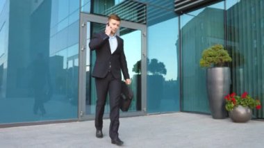 Genç işadamı telefonda konuşuyor ve şehir caddesinde yürüyor. Yakışıklı bir adam işe gidip geliyor ve dışarıda cep telefonuyla konuşuyor. Takım elbiseli adam dışarıda iş görüşmesi yapıyor. Yavaş çekim