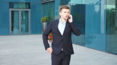 Genç işadamı telefonda konuşuyor ve başarıyı kutluyor. İş adamı cep telefonundan iyi haberler duymuş ve olumlu duygular besliyor. Erkek portresi başarıyla mutludur. Yavaş çekim