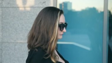 Şehir Ofis Binası yakınındaki sokak yürüyüş güneş gözlüklü genç iş kadını. Çekici işkadını çalışmaya commuting profil. Kendine güvenen kız iş doğru yolda olmak. Ağır çekim yakın çekim