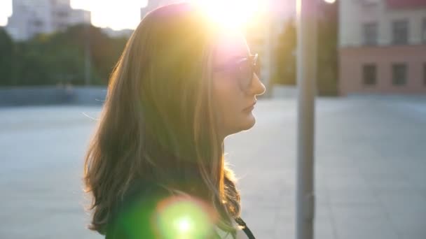 Profil av ung affärskvinna i solglasögon promenader i staden gatan. Attraktiva affärskvinna pendling till arbete med solen flare på bakgrunden. Självsäker tjej att vara på väg till jobbet. Närbild av långsamma mo — Stockvideo