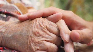 Genç erkek eli yaşlı bir eski kadın açık silah rahatlatıcı kapatın. Torun ve Büyükanne dışarıda birlikte vakit. Bakım ve sevgi kavramı. Yan görünümü ağır çekim