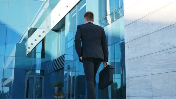 Un giovane uomo d'affari che va al lavoro. Il tipo sicuro di se 'in giacca e cravatta sta andando in ufficio. Uomo d'affari con una valigetta che cammina in strada vicino a un edificio moderno. Rallentatore Retrovisore Close up — Video Stock