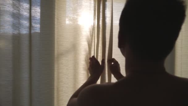 Uomo atletico irriconoscibile che apre le tende nella camera da letto dell'hotel e guarda fuori dalla finestra al mattino. Bello giovane ragazzo godendo bella vista nella giornata di sole. Retrovisore Close up rallentatore — Video Stock