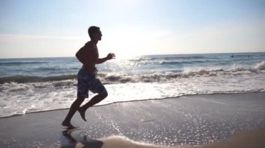 Deniz sahilde sabah koşan genç sportif adam. Sahil boyunca güneşli bir günde koşu atletik bir adam. Açık egzersiz erkek sporcu. Sağlıklı aktif yaşam tarzı. Yan görünümü ağır çekim