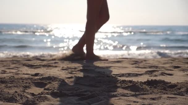 Kvinnliga fötter gå på sea beach på en solig dag med vågor på bakgrunden. Ben av ung kvinna kliver på sanden. Sommar semester eller semester koncept. Side view slowmotion närbild — Stockvideo