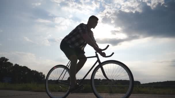 Silueta mladík na koni na vintage kolo s krásného západu slunce na obloze v pozadí. Sportovní chlap na kole v zemi silnici. Muž cyklista jízdní kolo. Zdravý aktivní životní styl zpomalené — Stock video