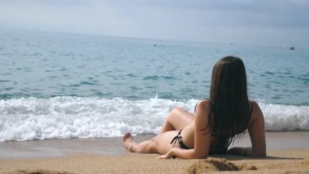 Junges Mädchen im Bikini am Strand liegend und sonnenbaden. schöne, unkenntliche Frau, die sich während der Sommerurlaubsreisen an der Küste entspannt. Konzept der Erholung an der Küste des Resorts. Rückansicht langsam mo — Stockvideo