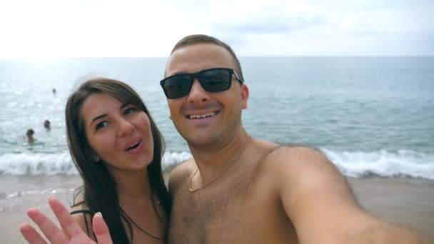 Młoda para szczęśliwy biorąc autoportret na plaży. Uśmiechający się para robi selfie na brzegu oceanu. Wesoły mężczyzna i kobieta korzystających wakacje honeymoon i zabawy nad morzem. Pojęcie odpoczynku — Wideo stockowe