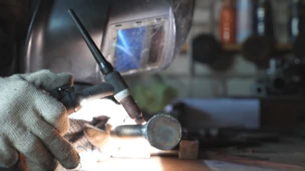 Close-up de soldador fazendo trabalho de soldagem usando equipamentos profissionais e máscara protetora na garagem ou oficina. Homem solda peças de metal. Flashes de trabalho de soldagem interior. Movimento lento — Vídeo de Stock