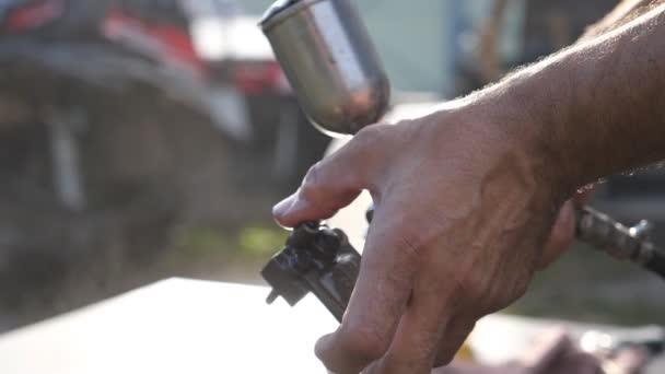 Ręce mechanika myje szczegółów samochodu przez rozpylanie wody. Człowiek używa sprayem do jego pracy. Osoba zajmująca się naprawami pracy na zewnątrz. Niewyraźne tło. Dołu widok zwolnionym tempie z bliska — Wideo stockowe