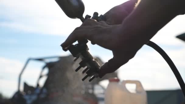 Le mani di meccanico lavano il dettaglio d'auto spruzzando l'acqua su esso. L'uomo usa il flacone spray per il suo lavoro. Riparatore che lavora all'aperto. Sfondo sfocato. Vista dal basso rallentatore Close up — Video Stock