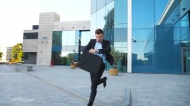 Evrak çantası ile genç işadamı çalışır ve saatine görünüyor. Kendine güvenen adam toplantı için geç. Yakındaki modern Binası takım elbise koşu başarılı adam. Yakışıklı adam acele randevu için. Ağır çekim