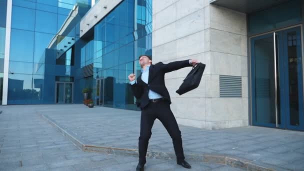 Caddenin üzerinde iyi bir anlaşma, takım elbiseli Genç mutlu işadamı sevinir. Başarılı ofis çalışanı evrak çantası ile modern building yakınındaki zafer dansı yapıyor. Yakışıklı adam başarı zevk. Ağır çekim — Stok video