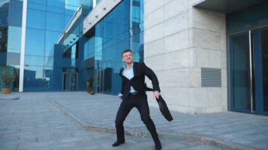 Caddenin üzerinde iyi bir anlaşma, takım elbiseli Genç mutlu işadamı sevinir. Başarılı ofis çalışanı evrak çantası ile modern building yakınındaki zafer dansı yapıyor. Yakışıklı adam başarı zevk. Ağır çekim