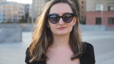 Şehirde sokak yürüyüş güneş gözlüklü genç işkadını portresi. Kameraya bakarak çekici bir iş kadını. Kendine güvenen kız çalışmaya commuting yüzü. Arka plan bulanık. Yavaş hareket kapatmak