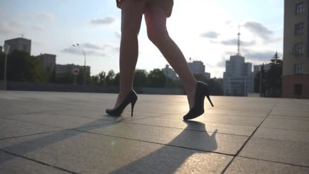 Vékony női lábak fekete cipőben magassarkúban sétálnak a főtéren naplementekor. Egy fiatal üzletasszony lábai magas sarkúban a városi utcában. Alacsony látószög Lassú mozgás Bezárás — Stock videók