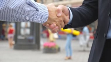 Bulanık şehir arka plan ile el sıkışan iki genç erkek arkadaşları. Kentsel ortamda birbirlerini tebrik emin iş adamları. Karşılıklı iş ortakları açık. Ağır çekim yakın çekim