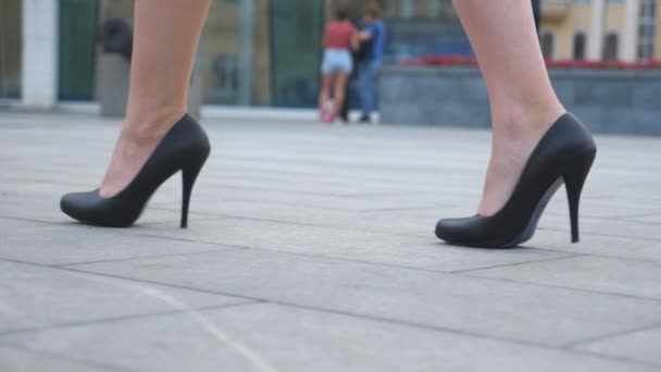 Egy fiatal üzletasszony lábai magas sarkúban a városi utcában. Vékony női lábak fekete cipőben, magassarkúban, a városban sétálva. Egy lány, aki dolgozni megy. Alacsony látószög Lassú mozgás Bezárás — Stock videók