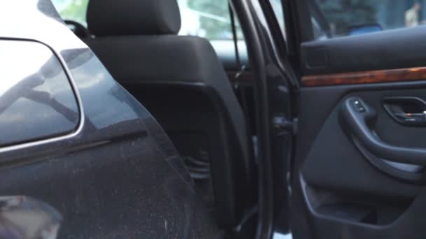 Mano de hombre de negocios abre y sostiene la puerta del coche para la mujer joven y hermosa. Hombre abriendo puerta de automóvil para pasajera. La mujer de negocios entra en el auto. Primer plano: cámara lenta — Vídeo de stock