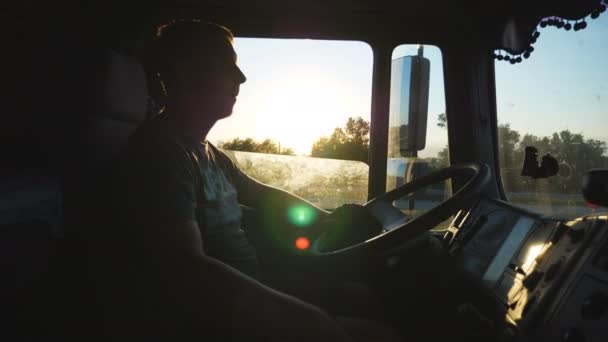 Homme conduisant un camion et surveillant attentivement la route. Caucasien gars est à cheval à travers la campagne sur le fond du coucher de soleil. Profil du chauffeur de camion à l'intérieur de la cabine. Vue latérale Mouvement lent Fermer — Video